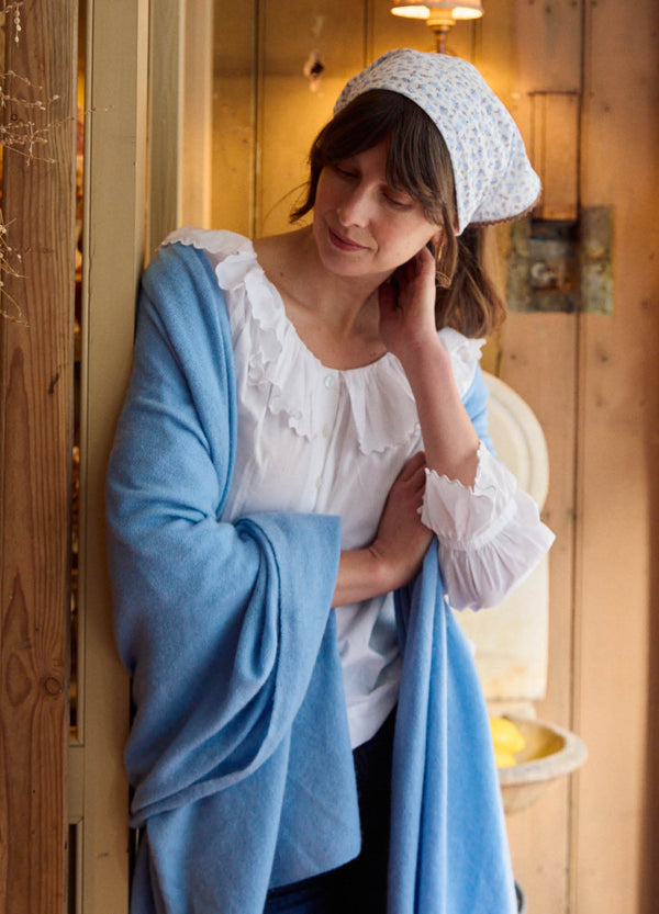 Woman in a white blouse and blue cardigan standing in a wooden interior setting.